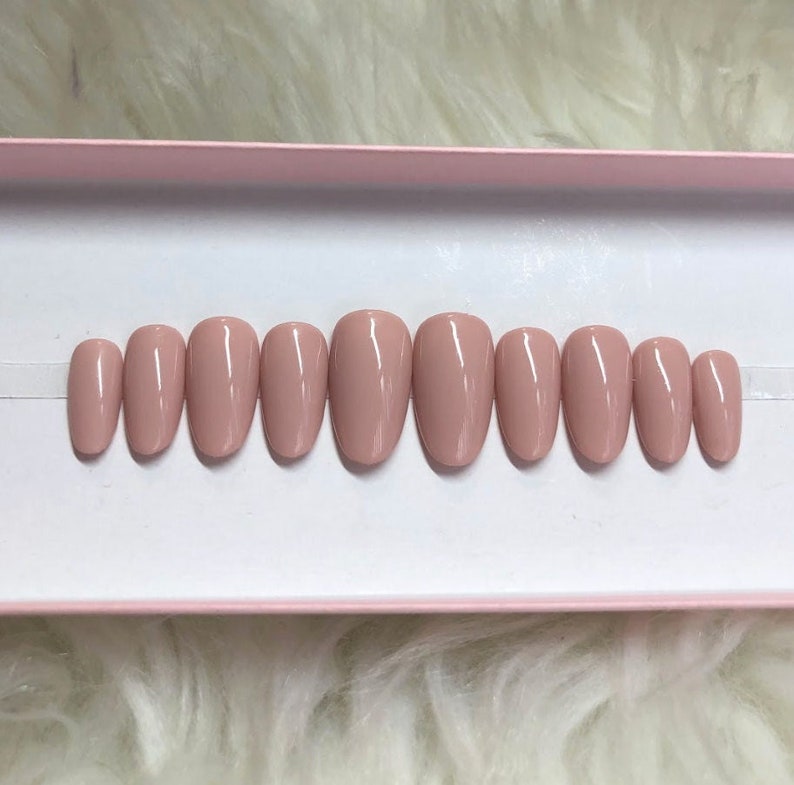 May include: A set of ten nude-colored oval-shaped fake nails in a pink box.