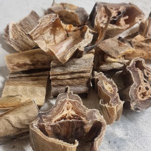 May include: A close-up of a pile of dried fish, with a light brown color and a rough texture. The fish is broken into pieces and has a slightly translucent appearance.