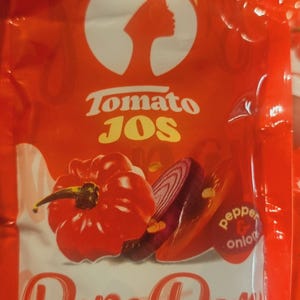 May include: A red packet of "Tomato Jos" tomato seasoning mix. The packet features a graphic of a red bell pepper, sliced red onion, and the words "Pepe Dem". The text "pepper & onion" is also visible.