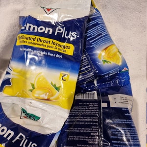 May include: Several crumpled packages of Vicks Lemon Plus medicated throat lozenges. The packages are white and blue with yellow text and a lemon graphic. Text includes "Medicated throat lozenges" and "Vitamin C."