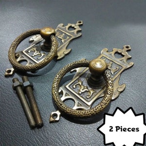 May include: Two ornate brass door handles with a ring pull and decorative details. The handles come with two screws for installation. 2 Pieces.