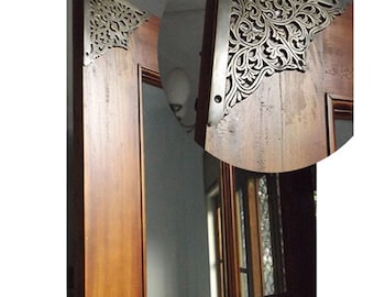 May include: A close-up of a wooden door with ornate metal corner accents. The accents are in a floral design and are a silver color.