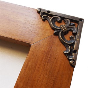 Puede incluir: Primer plano de un marco de fotos de madera con adornos de esquina de metal ornamentado. El marco es de un color marrón intenso y los adornos metálicos son de un color dorado bronceado.