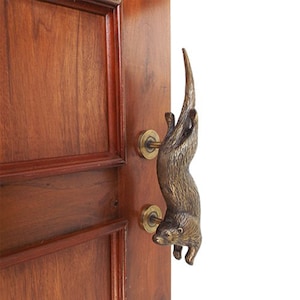 May include: A bronze door handle shaped like an otter, with the otter's tail extending up and the otter's head facing down. The handle is mounted on a wooden door.