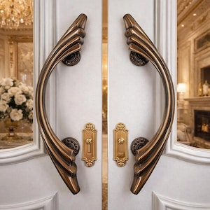 May include: A pair of large, curved, bronze-toned metal door handles with a ribbed, wing-like design mounted on white double doors. Each handle features circular mounting plates and a separate, rectangular brass-toned keyhole escutcheon plate.