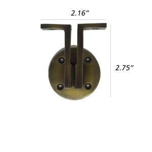 May include: A bronze-coloured metal cabinet pull with a circular base and two L-shaped arms. The pull measures 7 cm high and 5.5 cm wide.