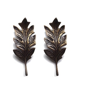 May include: A pair of gold-toned metal leaf-shaped earrings. The leaves have a detailed design and a slightly textured finish.