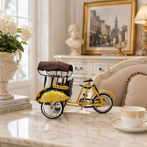 Pode incluir: Um modelo decorativo de metal de um riquixá amarelo com capota de tecido castanho, detalhes de estrutura preta e rodas raiadas. O compartimento de passageiros amarelo tem padrões azuis e prateados e inclui um pequeno assento.