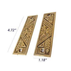 May include: Two brass-coloured rectangular decorative plates with detailed floral and geometric designs. Each plate is 12 cm long and 3 cm wide, with mounting holes. The plates have a vintage or antique appearance.