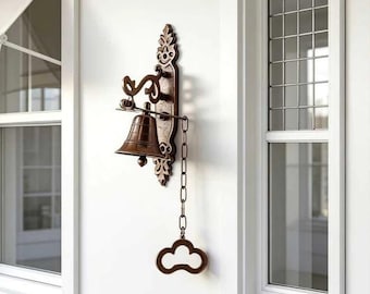 May include: A wall-mounted bronze-toned metal bell featuring an ornate, elongated backplate with decorative scrollwork. The bell hangs from a curved arm and includes a vertical metal chain attached to a cloud-shaped pull handle for ringing.