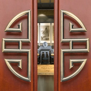 May include: A pair of wooden doors with ornate brass hardware featuring a traditional Chinese knot design. The doors are a rich reddish brown color and the hardware is a polished gold.