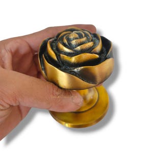 Può includere: Una maniglia per porta a forma di rosa dorata con una base rotonda. La maniglia ha un design dettagliato e testurizzato.