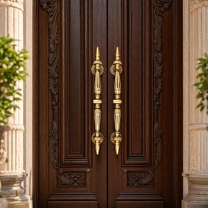 Puede incluir: Primer plano de una puerta doble de madera marrón oscuro con tallas ornamentadas y dos manijas doradas. Las manijas tienen un diseño decorativo y están alineadas verticalmente.