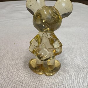 K&ouml;nnte beinhalten: Eine klare, gelblich get&ouml;nte Mickey Mouse-Figur. Die Figur steht, mit gro&szlig;en runden Ohren und einem kleinen Hut. Die Figur besteht aus transparentem Material, der Sockel ist herzf&ouml;rmig.