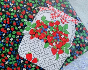 May include: A white basket filled with red strawberries and white flowers with green leaves. The basket has a red and white checkered bow. The basket is on a black background with a repeating pattern of red strawberries and white flowers.