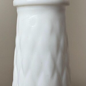 May include: A white, textured vase with a wavy pattern and a scalloped rim. The vase has a cylindrical shape and is made of a solid, opaque material. The design is simple and elegant, suitable for displaying flowers or as a decorative piece.