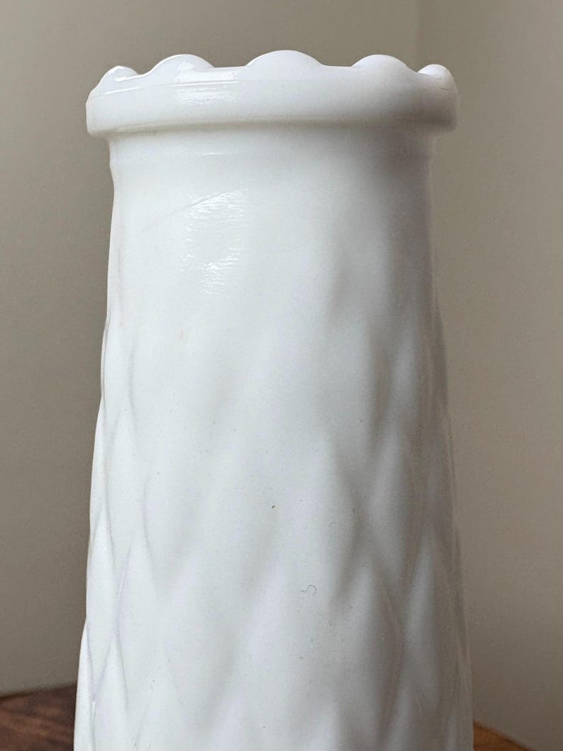 May include: A white, textured vase with a wavy pattern and a scalloped rim. The vase has a cylindrical shape and is made of a solid, opaque material. The design is simple and elegant, suitable for displaying flowers or as a decorative piece.