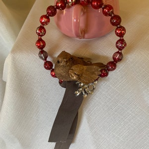 May include: A red beaded wreath with a brown bird and a brown ribbon. The wreath is decorated with gold flecks.