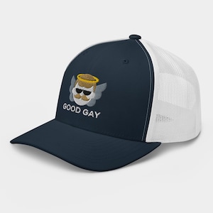 May include: Navy blue trucker hat with a white mesh back. The front features an embroidered design of a cartoon angel with sunglasses, a mustache, and the text "GOOD GAY" in white.