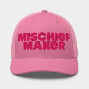 May include: A pink trucker hat featuring the embroidered text "MISCHIEF MAKER" in a darker pink. The hat has a mesh back and a curved peak. A playful accessory.