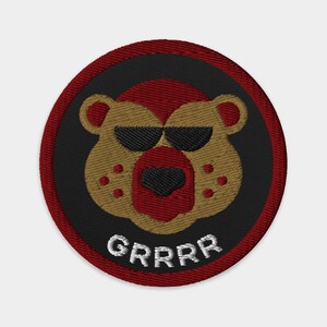 Puede incluir: Un parche bordado rojo, negro y dorado con un oso de dibujos animados que lleva gafas de sol y la palabra "GRRRR" debajo.