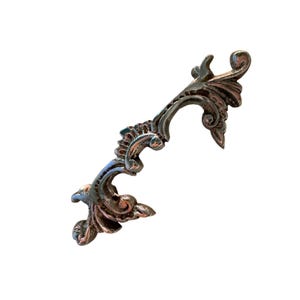 May include: Ornate, antique-style cabinet pull handle in a bronze finish. The handle features a scrolling, floral design with intricate details. The hardware is likely made of metal and is suitable for furniture restoration or decorative projects.