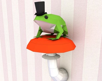 Könnte beinhalten: Ein Papierfrosch mit schwarzem Zylinder, der auf einem leuchtend roten Pilz sitzt. Der Frosch ist grün mit weißen Akzenten, der Pilz hat einen weißen Stiel. Der Hintergrund zeigt rosa und weiße Streifen.