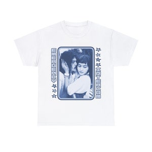 May include: White t-shirt with a blue graphic of a couple kissing. The graphic is framed with a blue border and stars. The text "EMERGENCY INTERCOM" is on the left and right sides of the graphic.