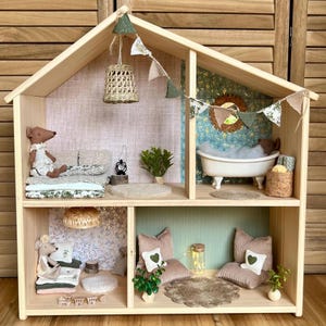 Puede incluir: Una casa de muñecas de madera con varias habitaciones, amueblada con objetos en miniatura. Las habitaciones incluyen un dormitorio, una sala de estar y un baño, cada una con un estilo distinto. La casa de muñecas está decorada con pequeños elementos decorativos, como una lámpara colgante y banderines.