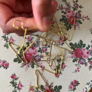 K&ouml;nnte beinhalten: Ein Haufen goldfarbener Miniatur-Kleiderb&uuml;gel, wahrscheinlich f&uuml;r Puppenkleidung oder Bastelprojekte.