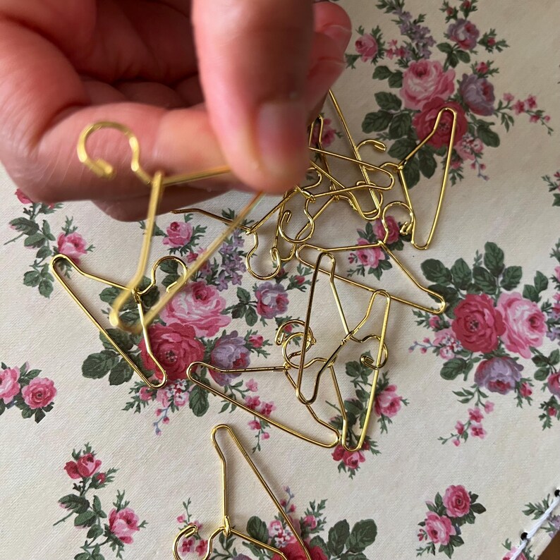 K&ouml;nnte beinhalten: Ein Haufen goldfarbener Miniatur-Kleiderb&uuml;gel, wahrscheinlich f&uuml;r Puppenkleidung oder Bastelprojekte.