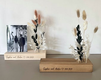 Könnte beinhalten: Zwei Holzbilderrahmen mit Trockenblumen und einem Schwarzweißfoto eines Paares. Die Rahmen sind mit dem Text "Sophie und Andre" und dem Datum "10.06.2023" graviert.