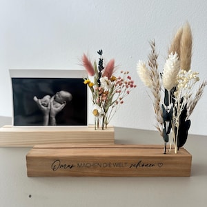 Könnte beinhalten: Holz-Foto- und Blumendisplay. Das Display zeigt ein schwarz-weißes Ultraschallbild, kleine Vasen mit Trockenblumen und eine Holzbasis mit dem Text "Omas machen die Welt schöner".