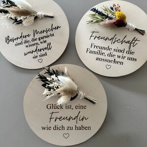 Peut inclure: Trois pancartes rondes en bois avec des fleurs séchées et des messages sincères. La première pancarte dit "Besondere Menschen sind die, die garnicht wissen, wie wundervoll sie sind". La deuxième pancarte dit "Freundschaft Freunde sind die Familie, die wir uns aussuchen". La troisième pancarte dit "Glück ist, eine Freundin wie dich zu haben".