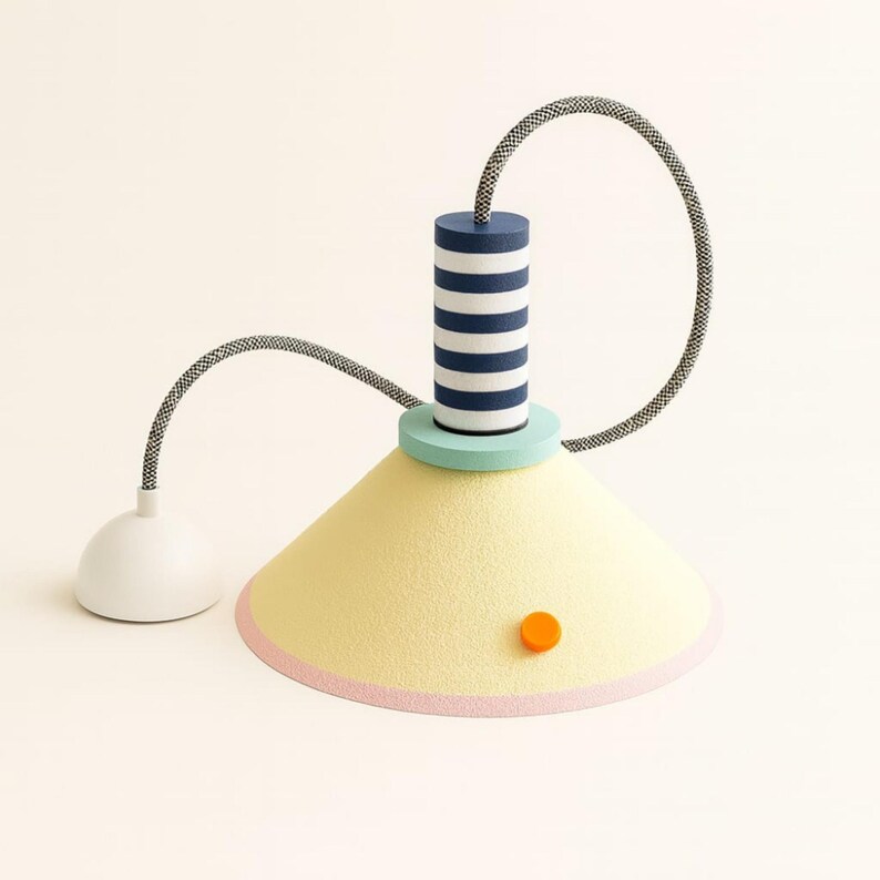 Op de afbeelding: Een hanglamp met een conische lichtgele kap met een roze onderrand en een klein oranje cirkelvormig accent. Het heeft een cilindrisch bovendeel met marineblauwe en witte horizontale strepen, een mintgroene basis en een zwart-wit snoer.