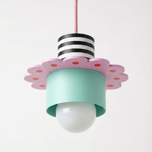 Può includere: Un'eccentrica lampada a sospensione con un paralume a forma di fiore. La lampada presenta una combinazione di colori rosa e verde menta, con una parte superiore a righe bianche e nere. La lampadina è di forma rotonda e bianca. Il cavo è rosa e bianco intrecciato.