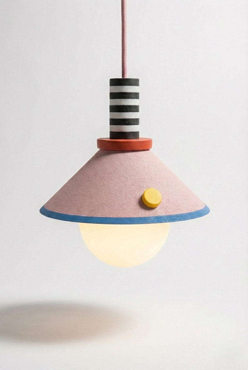May include: A modern pendant light with a pink shade, blue trim, and a yellow button. The light fixture has a striped black and white cylinder above a red disc. A spherical, glowing light bulb hangs below.