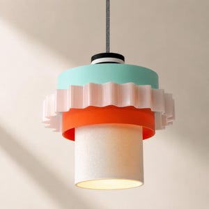 May include: A multi-tiered pendant light featuring a top mint green cylinder, a middle ruffled pale pink band, a lower orange ring, and a bottom white textured cylindrical shade. The fixture hangs from a black and white striped cap and a gray cord.
