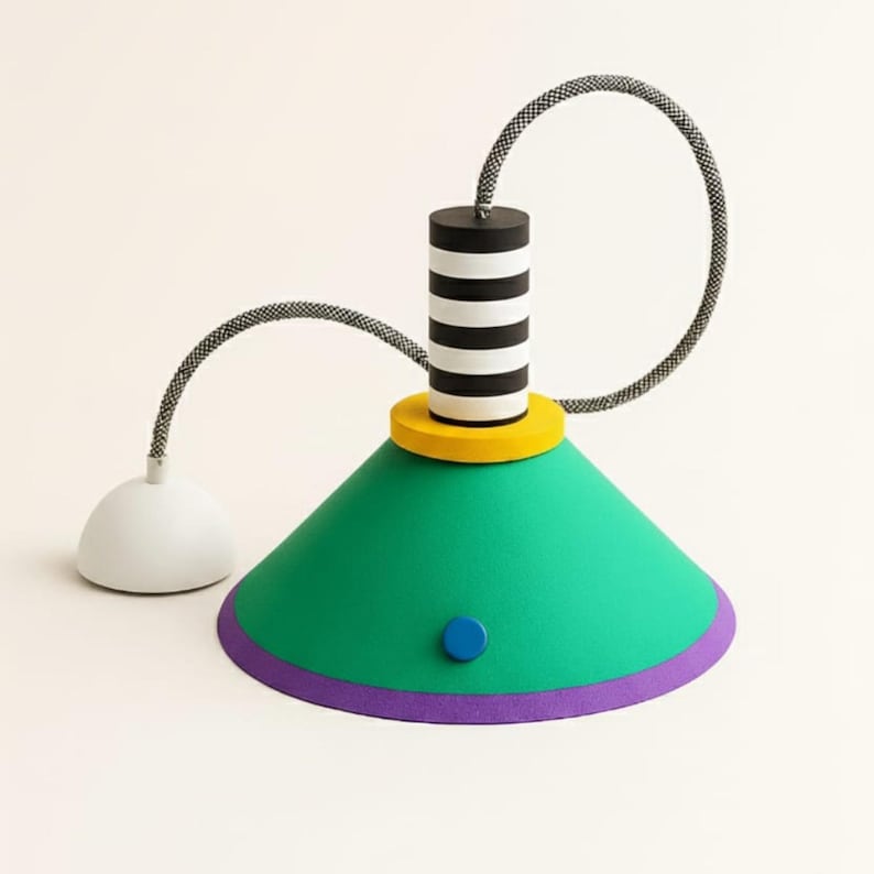 Op de afbeelding: Een hanglamp met een groene conische kap met een paarse rand, een gele ronde voet en een zwart-wit gestreepte cilindrische bovenkant. Een grijs stoffen snoer verbindt de kap met een witte koepelvormige plafondkap en een blauw accent.