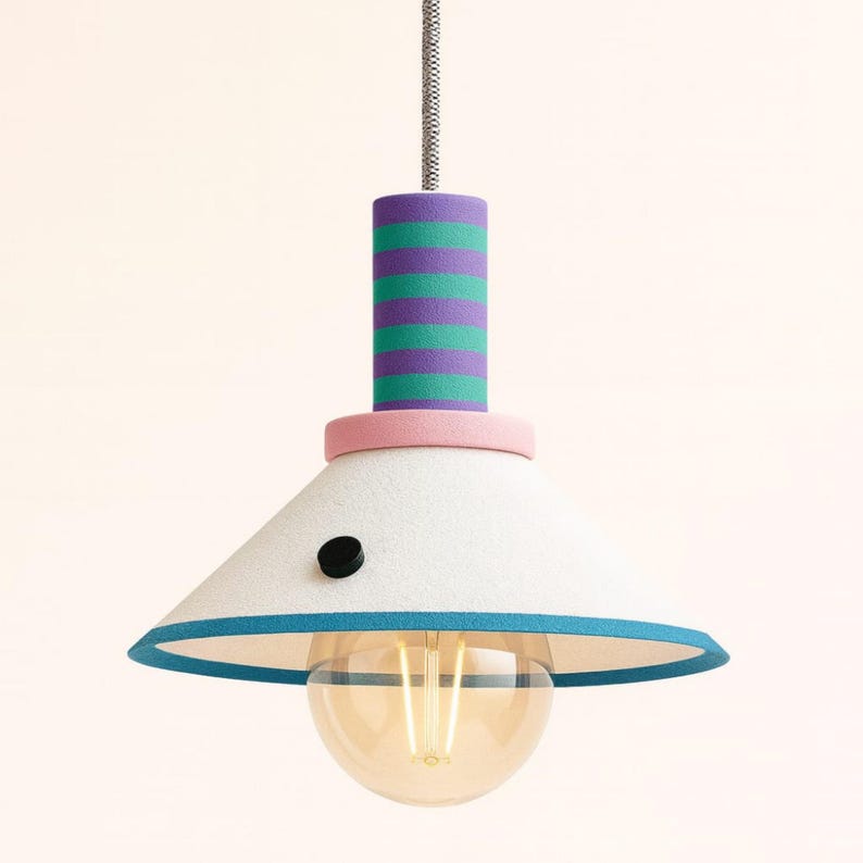 Op de afbeelding: Een hanglamp met een conische witte kap met een blauwgroene rand en een klein zwart rond accent. Het cilindrische bovendeel heeft horizontale paarse en blauwgroene strepen, gescheiden van de kap door een lichtroze ring.