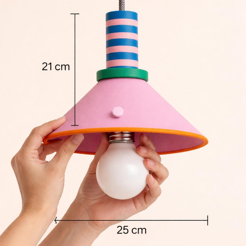 Op de afbeelding: Een hanglamp met een conische roze kap, een oranje rand en een blauw met roze gestreepte cilindrische bovenkant. De lamp heeft een groene sierring en een witte gloeilamp. De lamp is 21 cm hoog en 25 cm breed zoals aangegeven.