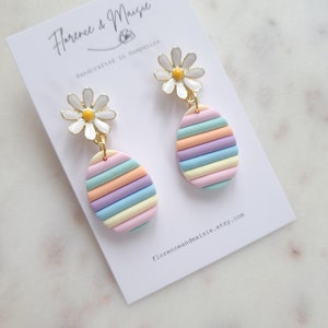 May include: A pair of pastel rainbow striped earrings with white daisy flower accents. The earrings are handcrafted in Hampshire.