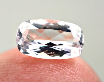 May include: A faceted, oval-shaped gemstone with a pale pink hue. The gem is held by a finger, showcasing its clarity and intricate cut. The gem's facets reflect light, creating a sparkling effect. The overall aesthetic is one of elegance and luxury.