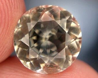 May include: A clear, faceted gemstone with a light brown hue. The gemstone is round and has a polished finish.