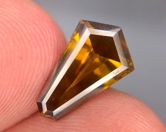 May include: A faceted, golden brown gemstone with a silver-toned bezel setting. The gemstone is cut in a unique, elongated shape.