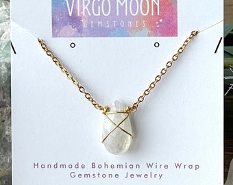 May include: A gold chain necklace with a white gemstone pendant wrapped in gold wire. The pendant is teardrop shaped. The necklace is displayed on a white card with the text "Virgo Moon Gemstones" and "Handmade Bohemian Wire Wrap Gemstone Jewelry".