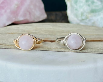 May include: Two wire wrapped rings with pink rose quartz stones. The ring on the left has a gold wire wrap and the ring on the right has a silver wire wrap.