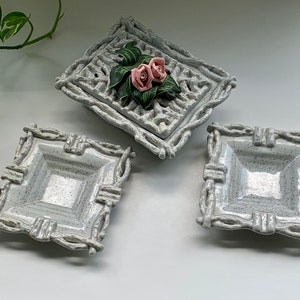 May include: Three white ceramic dishes with a raised, twig-like design around the edges. The center dish has a raised floral design with two pink roses.