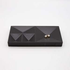 May include: A black concrete tray with a geometric design. The tray has multiple compartments and is perfect for holding small items like jewelry.