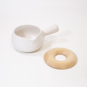 May include: A white ceramic creamer with a handle and a wooden ring. The creamer is designed to hold milk or cream for coffee or tea.